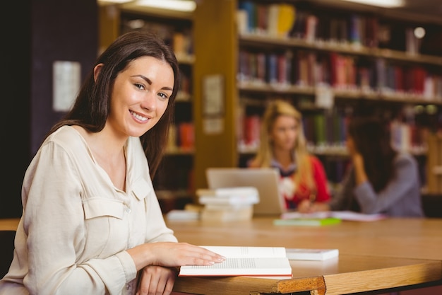 Studente sorridente che si siede allo scrittorio che legge libro di testo