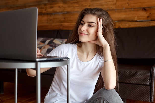 Studente sorridente felice attraente che ha chat video seduto sul pavimento, utilizzando il computer portatile