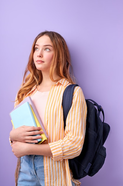 Studente teenager della ragazza caucasica in abbigliamento casual con zaino e libri isolati sulla porpora