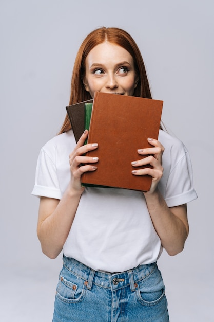 Studente universitario allegro della giovane donna che tiene libri e distoglie lo sguardo su fondo isolato