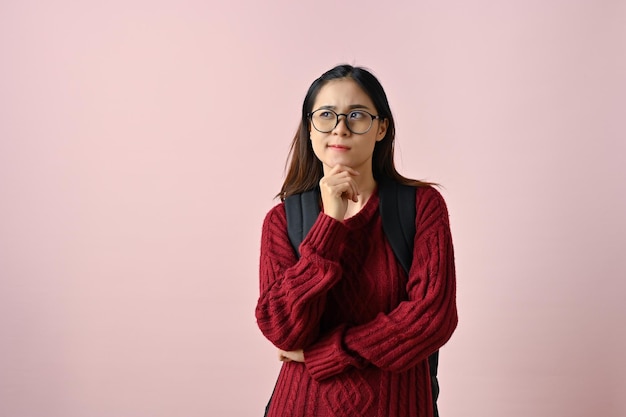 Studente universitario femminile asiatico pensieroso che tocca il suo mento che cerca trovare un'idea che pensa un piano
