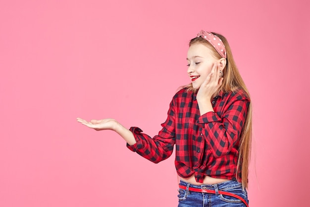 Studente universitario femminile caucasico in posa e punti con la mano. Giovane donna positiva su una parete rosa.