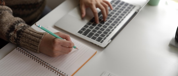 Studente universitario femminile che prepara le informazioni per la sua presentazione con il computer portatile e il taccuino in bianco