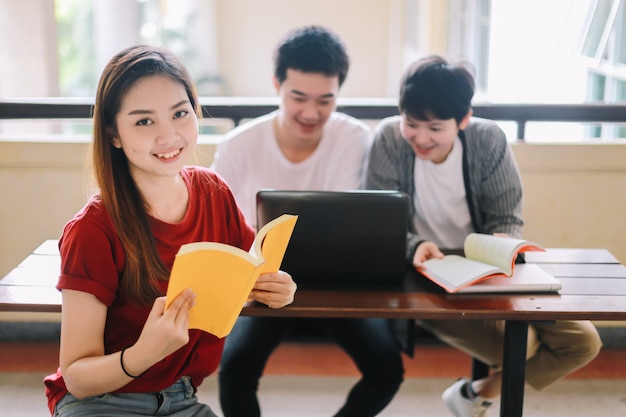 Studente universitario legge un libro di un amico con un portatile seduto in un edificio scolastico