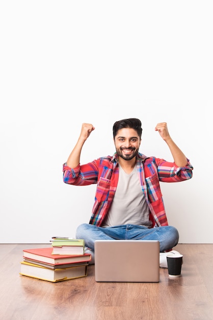 Studente universitario o universitario asiatico indiano che si siede con il computer portatile con i libri sul pavimento di legno contro il fondo bianco