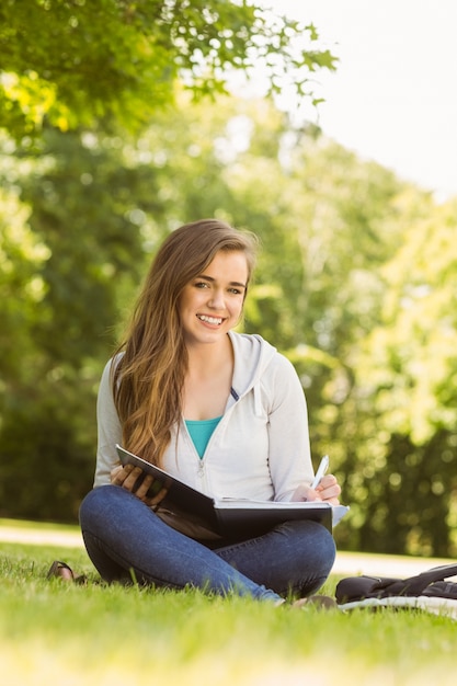 Studente universitario sorridente che si siede e che scrive sul blocco note