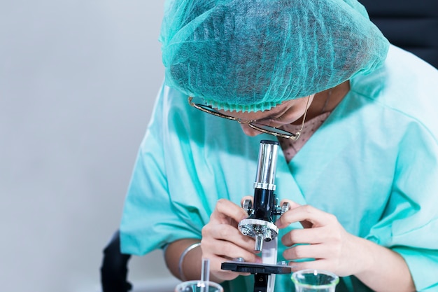 Studente veterinario della donna che guarda attraverso un microscopio vicino alla provetta per ricerca.