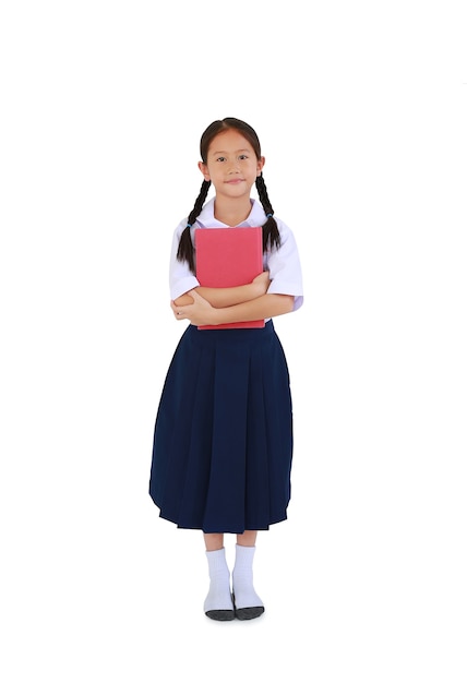 Studentessa abbastanza asiatica in uniforme scolastica tailandese in piedi con abbracciare un libro isolato su sfondo bianco. A tutta lunghezza con tracciato di ritaglio