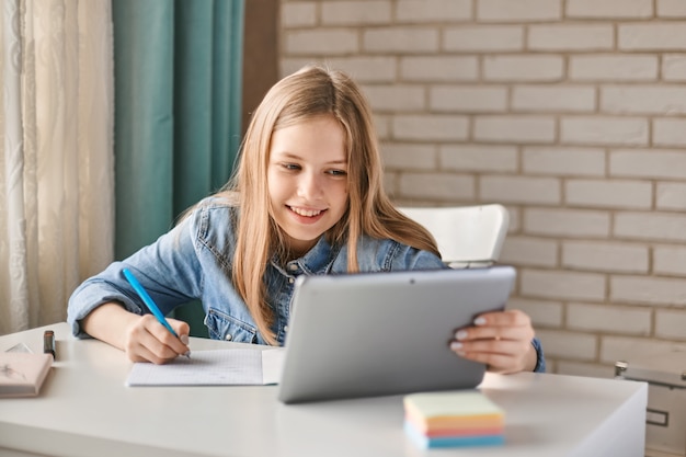 Studentessa adolescente carina fa i compiti con un tablet a casa.