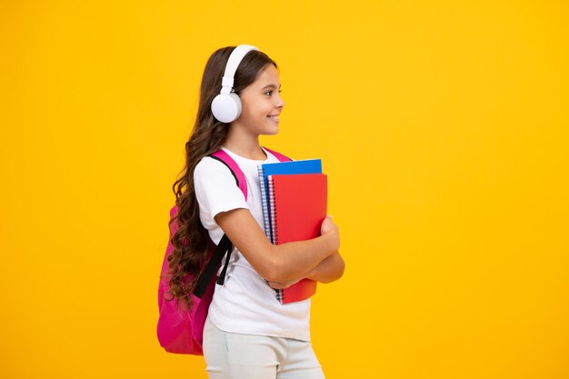 Studentessa adolescente studentessa in cuffia tiene libri su sfondo giallo studio isolato Concetto di educazione musicale e scolastica Ritorno a scuola