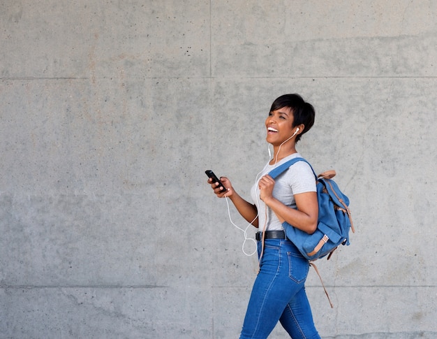 Studentessa africana che cammina con i trasduttori auricolari e lo Smart Phone