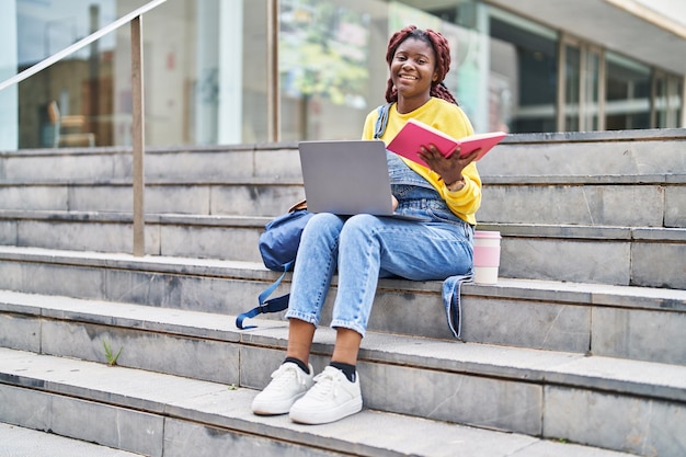 Studentessa afroamericana che utilizza il libro di lettura del computer portatile all'università