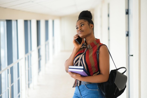 Studentessa afroamericana graziosa con lo zaino e le scartoffie all'aula dell'università