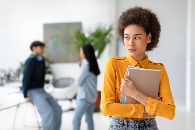 Studentessa afroamericana triste con quaderni in mano in piedi separatamente all'università