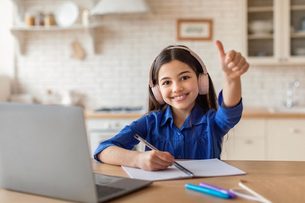 Studentessa al computer portatile che impara e gesturing i pollici in su a casa