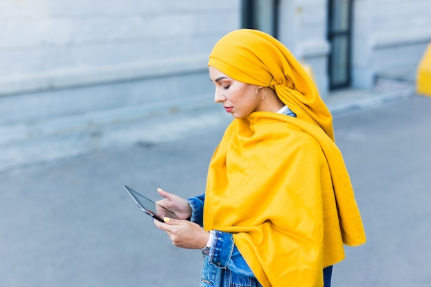 Studentessa araba. Bella studentessa musulmana che indossa il hijab giallo brillante che tiene compressa, spazio urbano