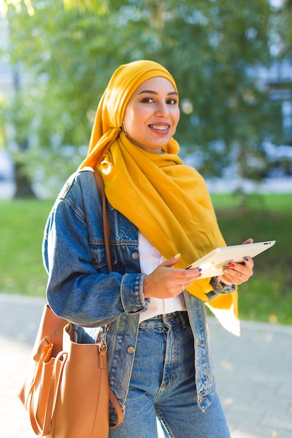 Studentessa araba. Bella studentessa musulmana che indossa tablet hijab giallo brillante.