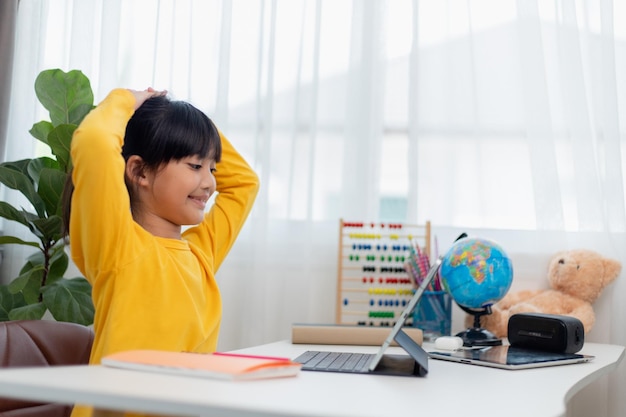 Studentessa asiatica che fa i compiti con il tablet digitale a casa I bambini usano i gadget per studiare Istruzione e apprendimento a distanza per i bambini Istruzione domiciliare durante la quarantena Resta a casa