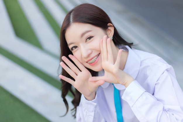 Studentessa asiatica in uniforme scolastica si alza e sorride felicemente con le parentesi graffe sui denti.