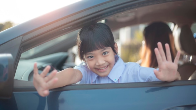 Studentessa asiatica pronta ad andare a scuola e salutando o salutando sullo sfondo dell'auto torna al concetto di scuola