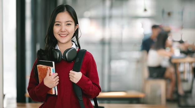 Studentessa asiatica sorridente che tiene libri in piedi in aula