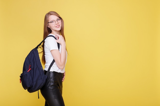 Studentessa attraente in bicchieri con zaino su una parete gialla