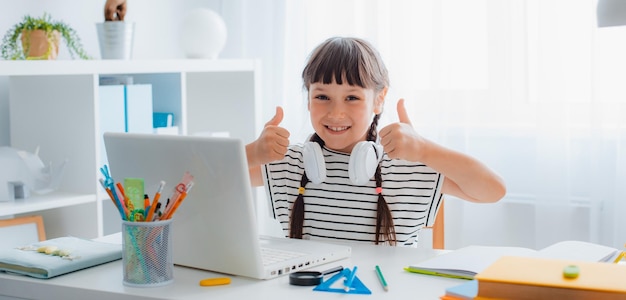 Studentessa bruna del bambino che studia i compiti durante una lezione online a casa in una stanza bianca luminosa concetto di istruzione online del tempo della scuola