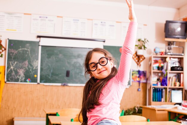 Studentessa carina con grandi occhiali divertenti, seduta sul desktop e sorridente