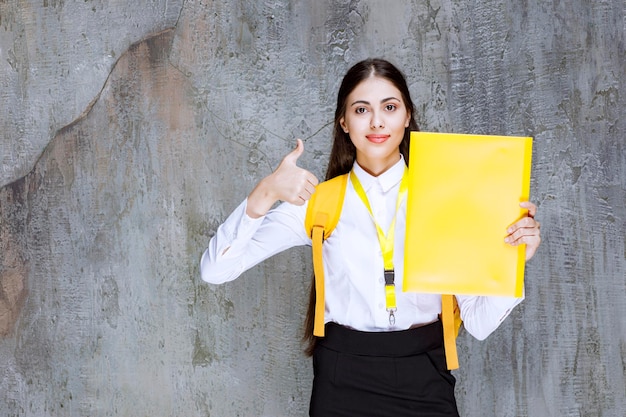 Studentessa che indossa il blocco note della tenuta dello zaino giallo. Foto di alta qualità