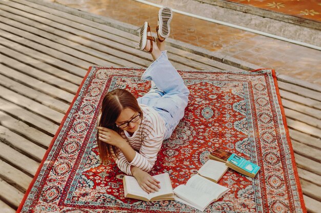 studentessa che legge un libro sdraiata sul pavimento su un tappeto in stile vintage