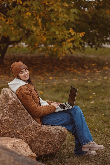 studentessa che naviga sul computer portatile e fa l'incarico mentre studia nel parco autunnale