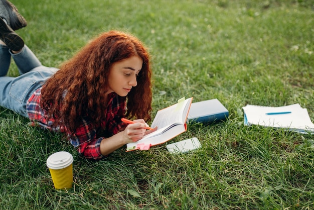 Studentessa che prepara per gli esami sull'erba nel parco estivo.