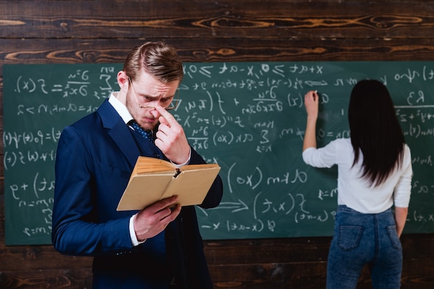 Studentessa che risolve l'equazione alla lavagna giovane insegnante con occhiali di regolazione a setole corte durante la lettura di un fischio