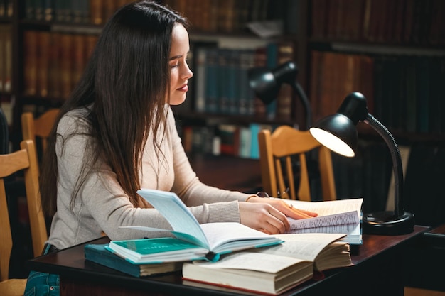 Studentessa che studia in biblioteca al tavolo con una lampada da scrivania