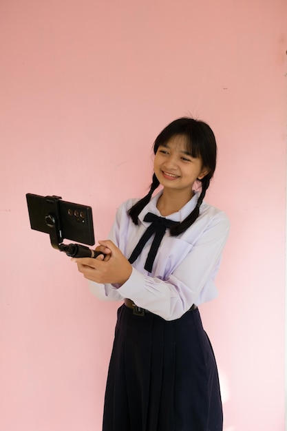 Studentessa che usa il cellulare e il selfie stick su sfondo rosa
