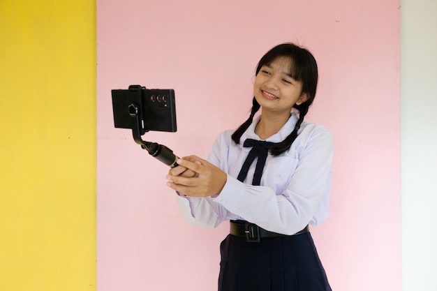 Studentessa che usa il cellulare e il selfie stick su sfondo rosa