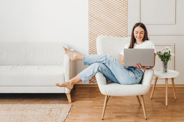 Studentessa che usa il computer portatile a casa donna seduta sulla sedia sorridente e guarda sul computer