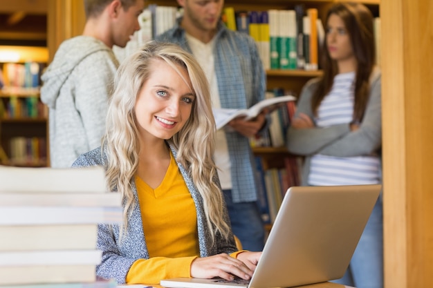 Studentessa che utilizza computer portatile mentre altre nella priorità bassa alla libreria