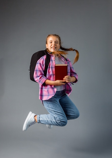 Studentessa con rbkzak che salta su uno sfondo grigio. contenuto scolastico