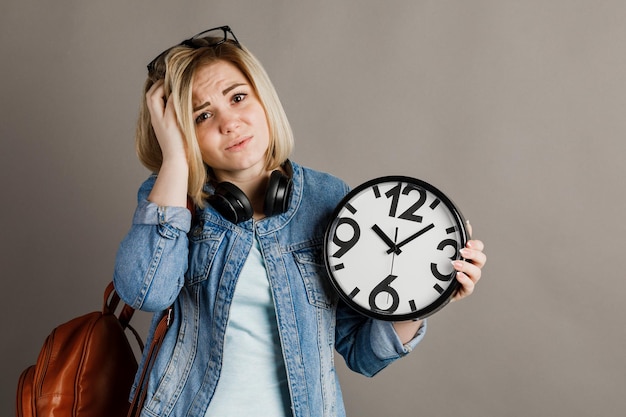 Studentessa con un grande orologio in mano su uno sfondo grigio