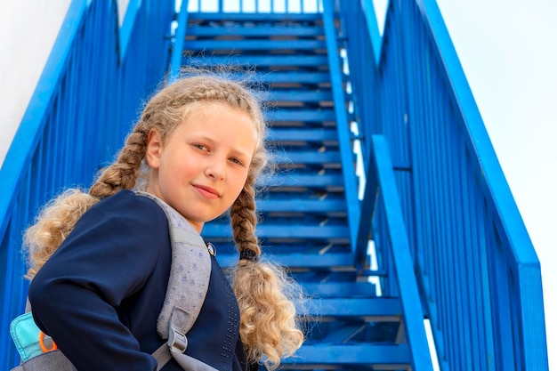 Studentessa con un sorriso sale le scale ragazza in uniforme con uno zaino Ragazza vicino alle scale