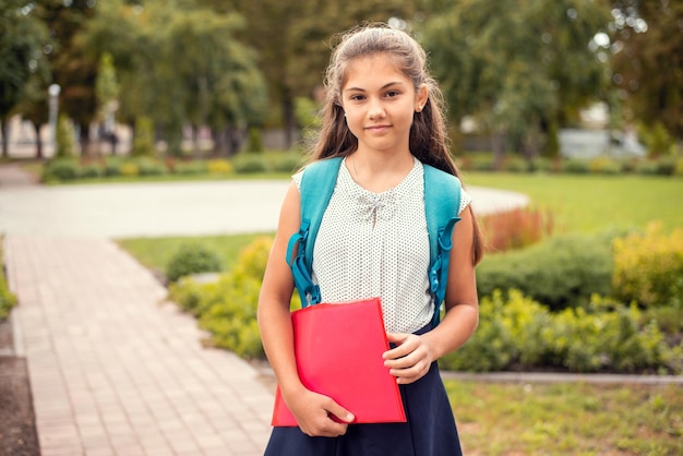 Studentessa con uno zaino e una cartella che va a scuola la mattina nel parco