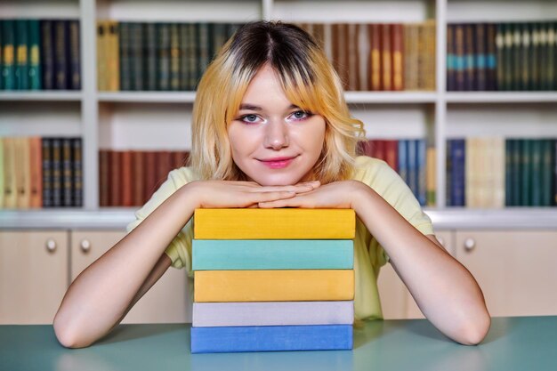 Studentessa di liceo adolescente femminile che guarda l'obbiettivo con libri in biblioteca