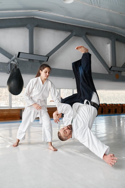 Studentessa di talento che lancia insegnante di aikido sul pavimento durante lo sparring e l'allenamento di autodifesa in palestra