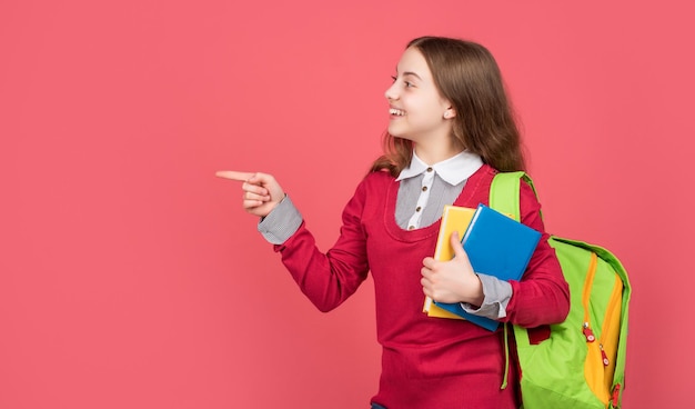 Studentessa felice con libri di scuola e borsa che punta il dito per l'educazione di sfondo rosso dello spazio della copia