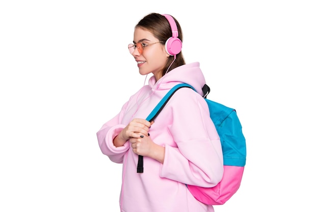 Studentessa felice in felpa con cappuccio rosa casual che ascolta il corso audio in cuffie che trasportano la borsa della scuola