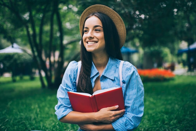 Studentessa felice nel libro di testo del cappello per l'istruzione e ridendo godendosi il tempo per l'hobby della letteratura