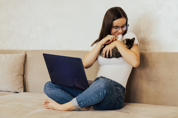 Studentessa freelance lavora a casa su un compito e gioca con il suo piccolo simpatico gatto