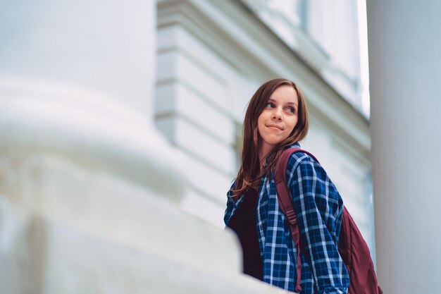 Studentessa fuori dall'edificio universitario Angolo basso della giovane donna con lo zaino che guarda lontano sopra la spalla mentre si trova sul portico dell'edificio universitario prima degli studi