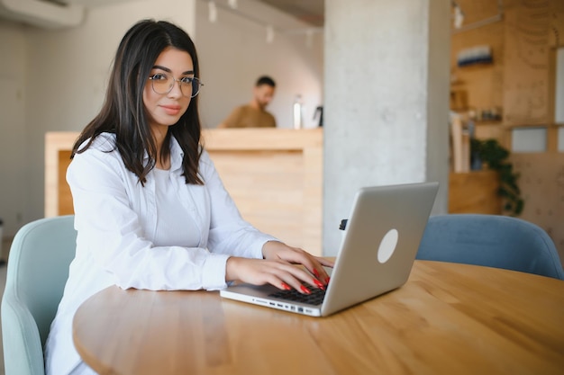 Studentessa gioiosa che studia online al bar utilizzando laptop e auricolari spazio vuoto